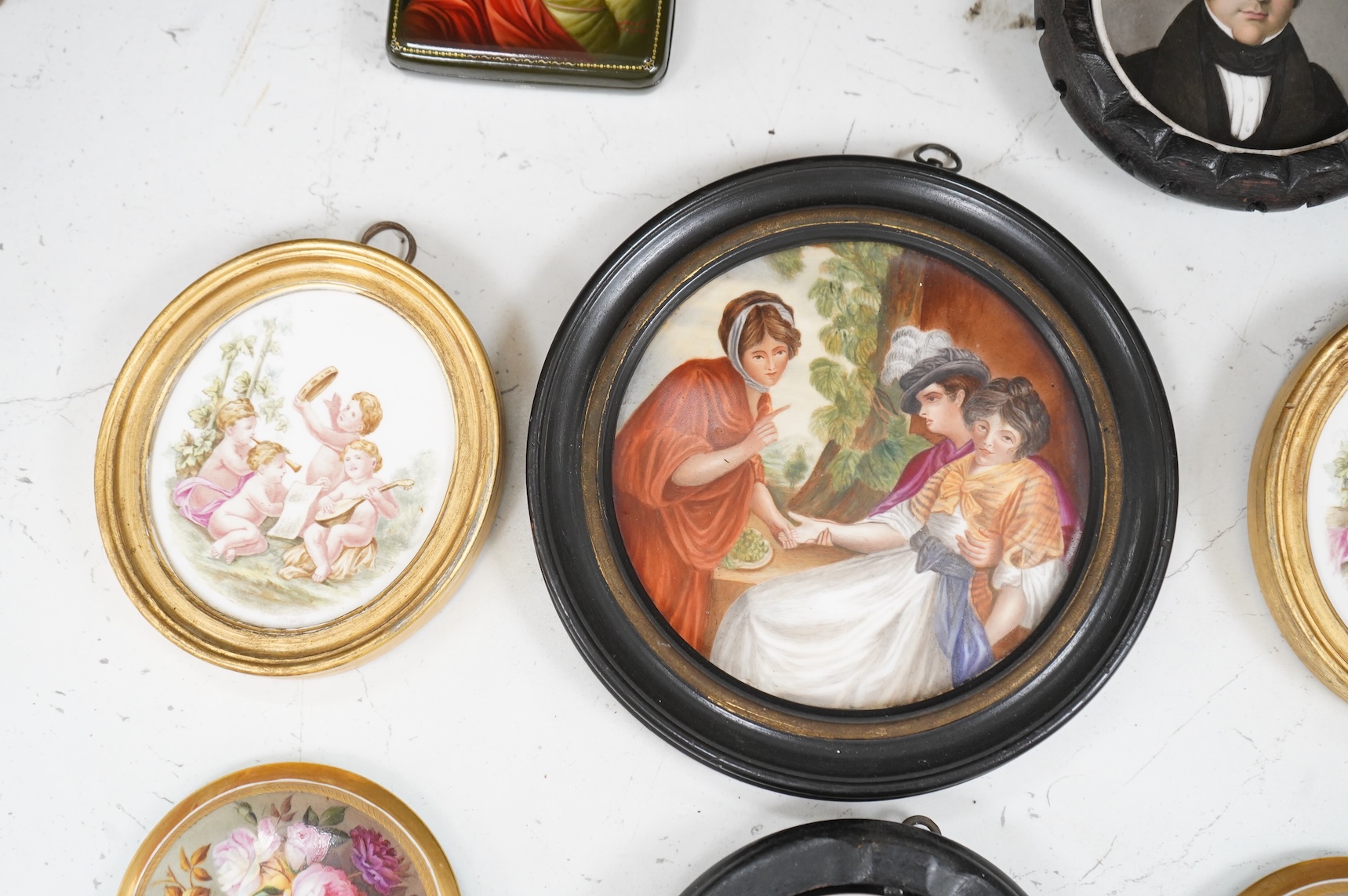 A collection of 19th century porcelain panels, pot lids and plaques to include a pair of hand painted floral lids, Russian lacquered box depicting a lady and a late 19th century Continental brass framed convex oval ename